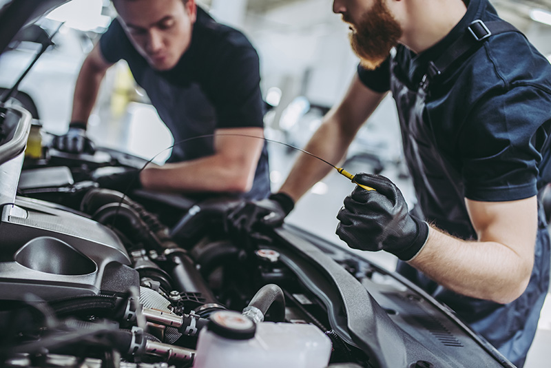 Two mechanics checking the engine oil of a car in an auto shop.