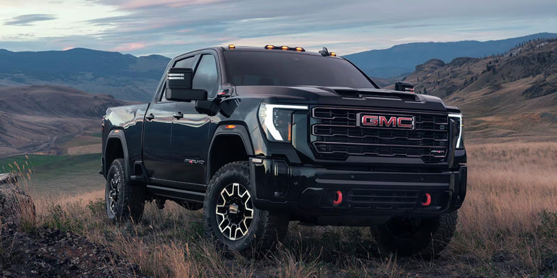 A black GMC truck parked on rugged terrain with mountains in the background
