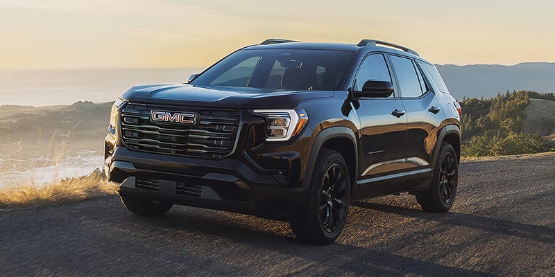 Black GMC Terrain SUV driving on a scenic road with a coastal landscape in the background.